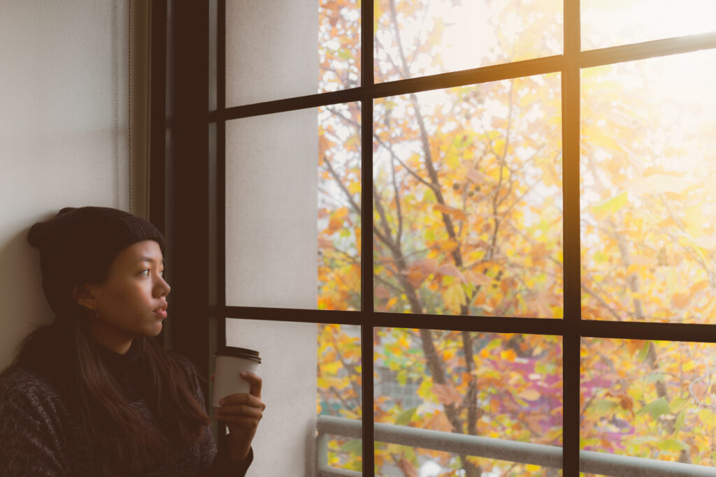 Woman looking out the window with a disposable cup of coffee in her hand